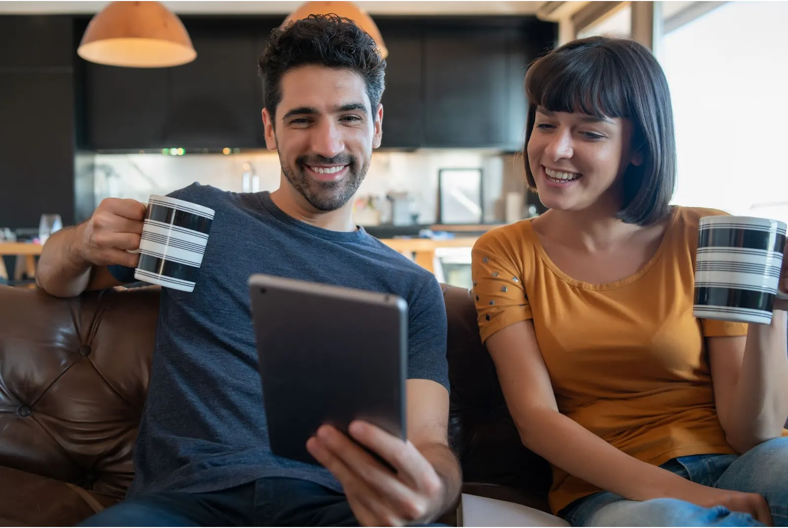 A smiling couple sits together, enjoying tea while browsing on a tablet, representing ease of use with ATT Internet Packages.