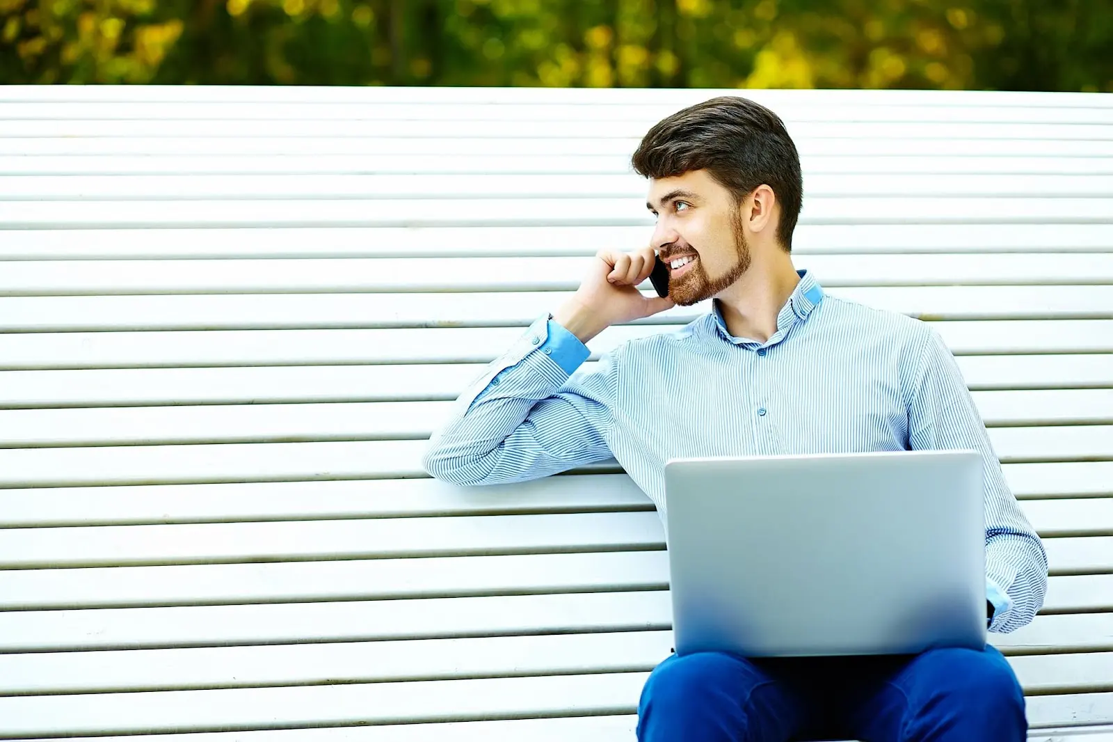 Man sitting on a garden bench using a smartphone and laptop, representing connectivity and remote access—related to Windstream services.